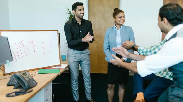 Colleagues joyfully applaud a new hire announcement in a modern office setting.
