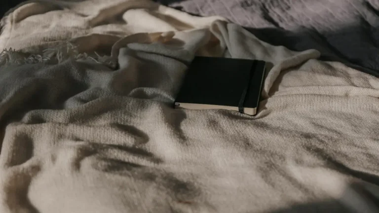 A closed black notebook resting on a textured cream blanket in natural light.