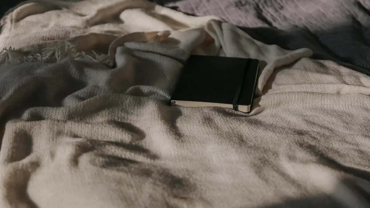 A closed black notebook resting on a textured cream blanket in natural light.
