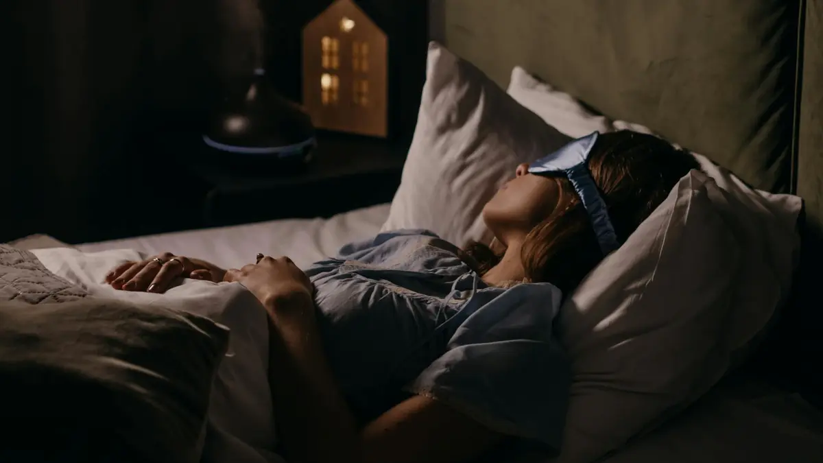 A woman peacefully sleeping with an eye mask in a dimly lit bedroom, capturing a serene bedtime atmo
