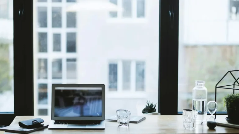 Sleek office desk setup featuring a laptop, glass of water, and open window view.