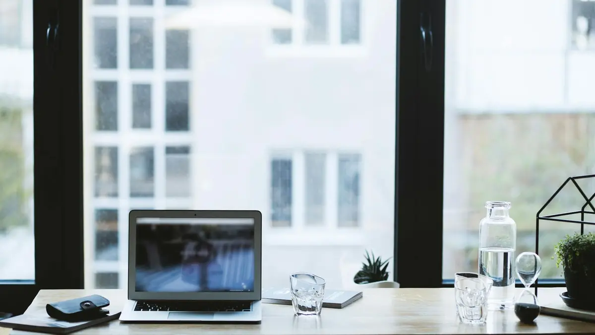 Sleek office desk setup featuring a laptop, glass of water, and open window view.